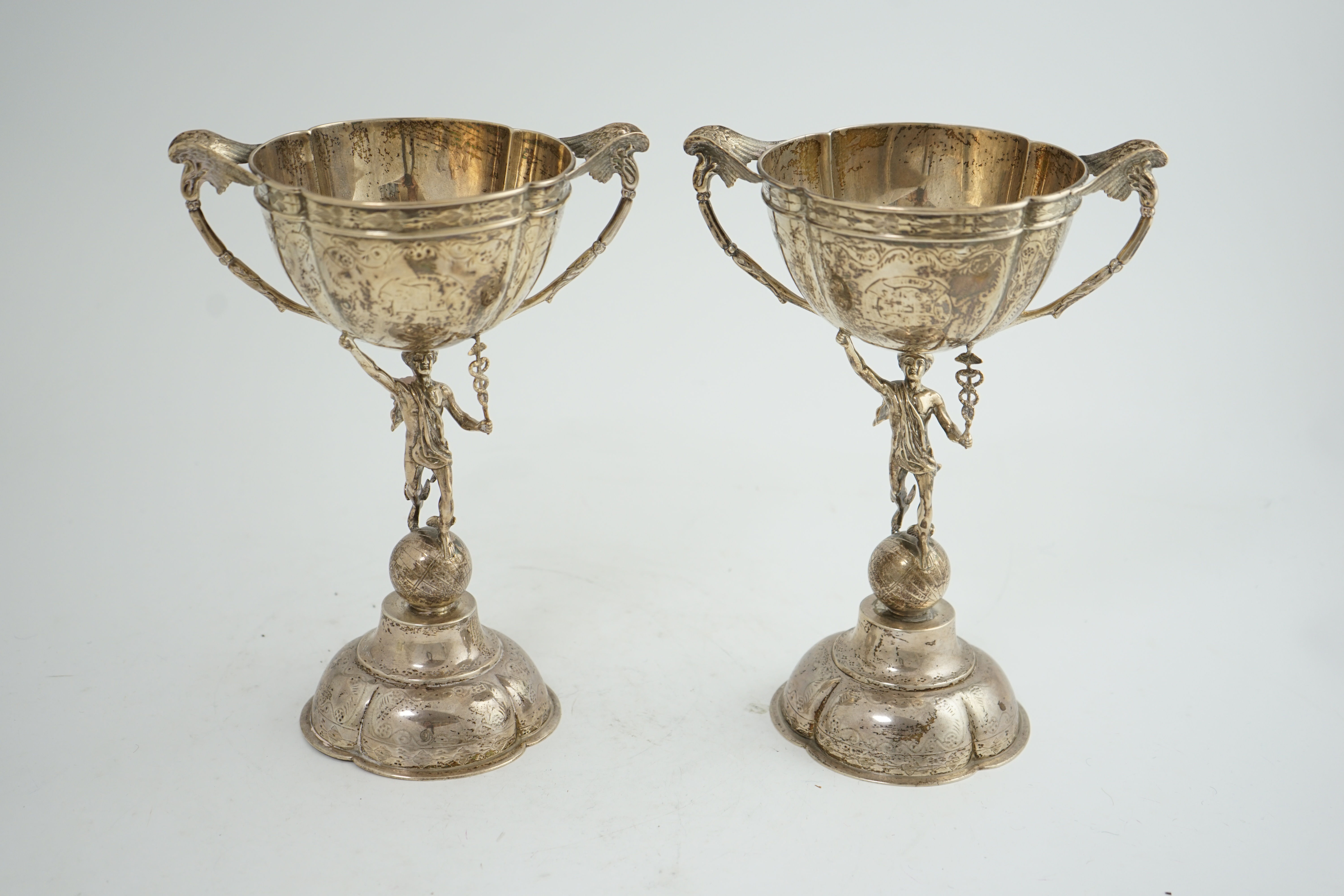 A pair of Victorian silver two handled pedestal cups, each figural stem modelled as Hermes upon a globe, by Edward Charles Brown